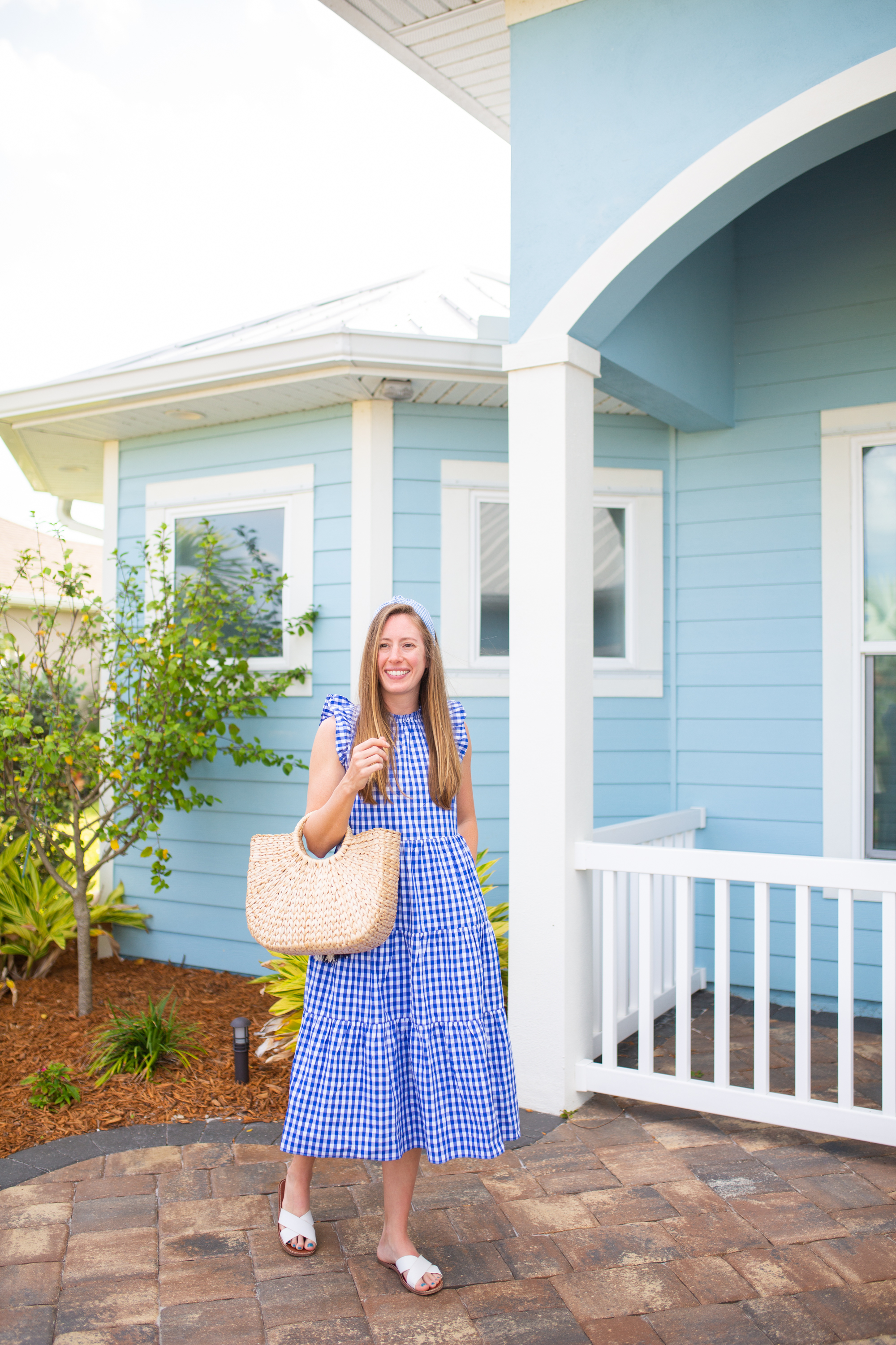 woman wearing J.Crew Gingham Tiered Dress in blue, holding a bag, and standing outside a blue house