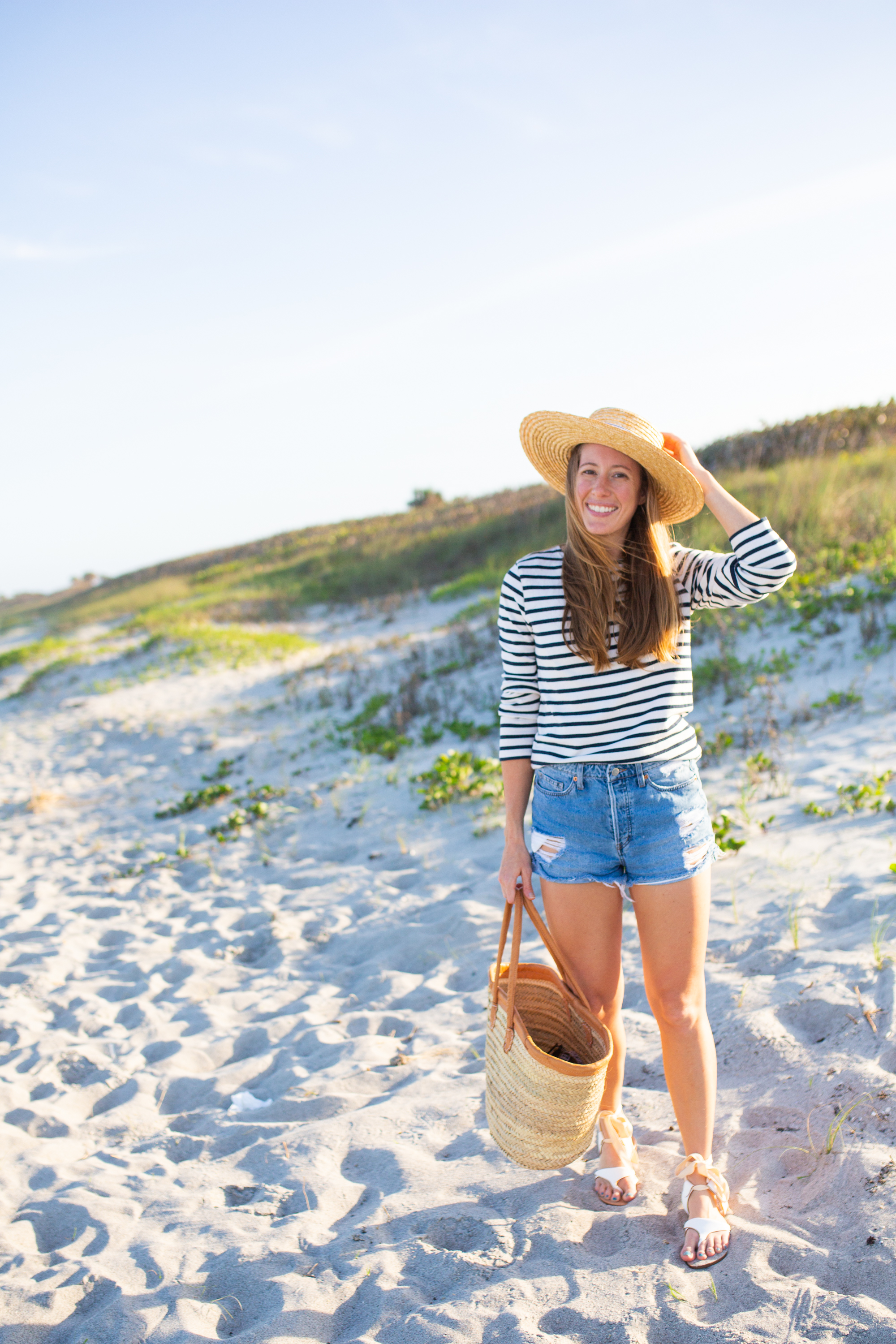 woman at the beach and holding her beach hat and bag to share Sarah Flint Grear Sandals Review